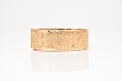 Lot 231 - A 9ct gold bright cut engraved hinged bangle